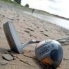 Golfschläger und Golfball liegen am Strand.